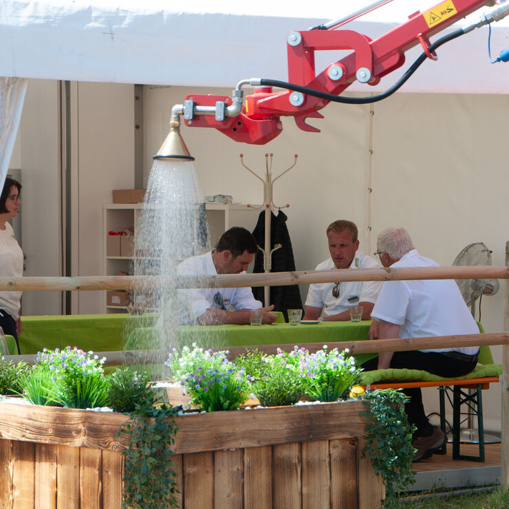 Demonstration einer Bewässerungslösung auf der demopark. Wasser wird über eine Düse auf eine bepflanzte Ausstellungsfläche verteilt, während Fachbesucher im Hintergrund Gespräche führen