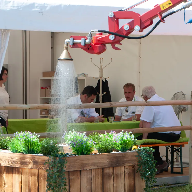 Demonstration einer Bewässerungslösung auf der demopark. Wasser wird über eine Düse auf eine bepflanzte Ausstellungsfläche verteilt, während Fachbesucher im Hintergrund Gespräche führen